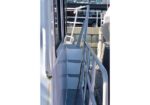 Metal gangway with rails on a boat, leading to a doorway and steps at a dockside area