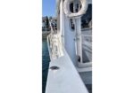Boat deck with a life preserver by the cabin door and a small fish on the white railing; water and a dock are in the background.