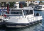 White motorboat docked at a marina, with railing and red umbrellas on the deck finshed by calm water.