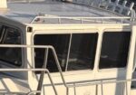 Front/upper cabin of a white vehicle (bus or van) with a metal roof rack and surrounding guard rails.