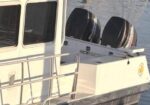 White passenger boat with two large outboard motors mounted on the stern beside calm water, railings in the foreground.