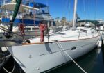 White sailboat docked at a marina with red mooring lines and other boats in the background on a sunny day