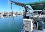 Sailboat at a marina with a Lifesling life-saving flotation device mounted on the stern, calm blue water and other boats in the background