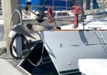 Sailboat docked at a marina with coiled red ropes and rigging on the deck; bow and anchor area visible.