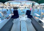 Cockpit of a boat with two blue captain's chairs, cushioned benches along the sides, a central steering wheel, and a marina full of moored boats in calm water.