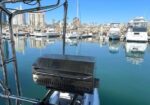 Stainless Magma grill mounted on a boat railing, overlooking a calm marina with moored boats and distant buildings.