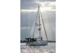 Sailboat with white sails and a small group on deck gliding across sunlit water, a US flag flying from the sail.