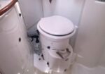 Compact marine toilet in a small boat head, with hose and bottle of cleaner nearby.