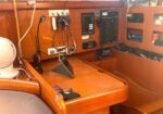 Sailboat navigation station with electrical panels, radios, and a tablet on a wooden desk area near the cabin wall.