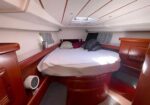 Wood-paneled boat cabin with a centered bed, pillows, and small side windows; skylight overhead.