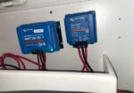 Two blue Victron solar power devices mounted on a white wall: left is a SmartSolar MPPT 100/50 charge controller with status LEDs, right is an Orion-XS DC-DC charger.