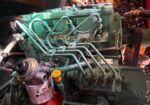 Close-up of a green diesel engine with many fuel lines and hoses; visible oil filter on the left and a yellow oil fill cap.