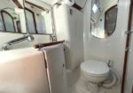 Compact boat head with a toilet, white sink, mirrors, wood trim, and a porthole window. (informative)