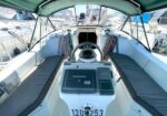Sailboat cockpit with steering wheel, Raymarine display, and cushioned benches, moored in a marina.