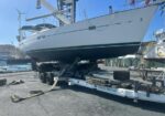 Sailboat on a trailer in a boatyard being lifted for maintenance, with a crane and spare parts nearby.