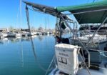 Marina scene with sailboats moored; foreground shows a Lifesling life-saving bag on a sailboat stern and a green shade canopy above.