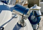 Close-up of a chrome spotlight mounted on a sailboat deck, with a blue hose and dock equipment in the background.
