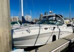 White motor yacht docked at a marina with city high-rises in the background on a sunny day.