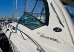 White Sundancer 340 motor yacht docked at marina with blue sky, cockpit windows, and stainless railing visible.