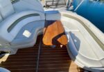 Curved white boat seating around a small wooden table on a teak deck by the water.