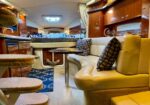 Cozy yacht cabin with curved beige sofa, round table, and nautical decor; stairs to a sleeping area in the background.