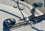 Boat bow with a heavy anchor chain and chrome cleat/fittings on a white deck, bathed in sunlight.