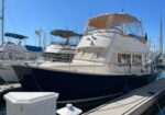 A white-and-navy motor yacht moored at a marina with other boats nearby, featuring a beige canvas canopy over the upper deck.