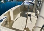 Open cockpit area of a beige boat with stairs and a stainless railing, moored at a marina with blue water in the background.