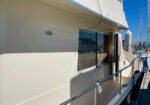 Cream-colored boat hull with a small '34' badge, cabin window, and open door, alongside stainless railings at a marina.