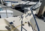 White motorboat at a marina with a yellow hose, railings, and other docked boats visible in the background, dock boxes nearby.