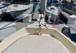 Bow view of a cream-colored motorboat docked at a marina; metal railing, cleats, and lines, with other boats and slips in the background.
