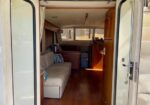 Interior of a boat cabin with a white sofa and blue cushions, wooden cabinets, and a helm at the far end.