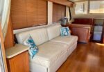 Cozy boat cabin living area with a white leather sofa, blue patterned throw pillows, wooden cabinets, and teak flooring.