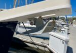 Sailboat hull at a marina with a large metal anchor hanging from the bow under a white platform, bright blue sky above.