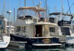 Motor yacht docked at a marina with a beige canopy, open rear door, and American flag, surrounded by sailboats.