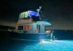 Nighttime yacht with blue lights on the water; glowing windows and dark shoreline in the background.