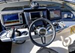 Boat cockpit at the helm with a steering wheel and multiple navigation screens on the dash.
