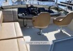 Open boat cockpit with beige lounge seating to port and two beige captain chairs at the helm; marina in the background.