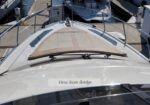 View from the bridge of a white motorboat looking toward the bow, deck hatch in the center and railings on both sides at a marina.