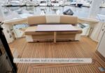 Teak-deck lounge area on a luxury yacht with a rectangular table, overlooking a marina full of moored boats.