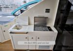 Aft deck BBQ and wet bar on a yacht, grill open, with sink and storage cabinets; marina in the background.