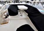 Yacht cockpit with white deck, center pedestal table, and seating covered in black fabric, marina in the background.