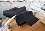 Yacht deck with two dark protective covers over seating areas, teak flooring, at a marina.