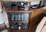 Wood bar cabinet with glass-front doors displaying wine glasses and glass racks in a home setting.