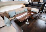 Luxurious yacht salon with an L-shaped beige seating area, light blue cushions, and a glossy wooden dining table on a pedestal base.