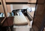 VIP guest cabin in a yacht: bed with blue and white pillows, wood cabinetry, and a small bedside table nearby.