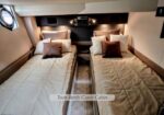 Twin berth guest cabin in a yacht with two single beds, brown and beige pillows, and a small central aisle.”​