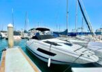 White luxury motor yacht docked at a marina, blue sky and other sailboats in the background.