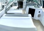 Open cockpit of a white motor yacht with cushioned seating, steering wheel, and galley; marina with moored boats in the background.