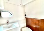 Tiny airplane lavatory with white cabinetry, a small sink, round window, and a closed toilet; wood-paneled wall on the lower half.